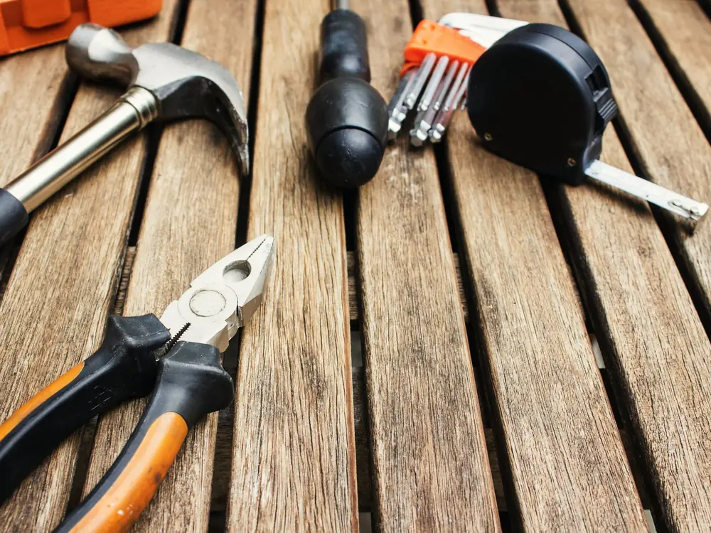 Hamer, tang, schroevendraaier en rolmaat op een houten vloer